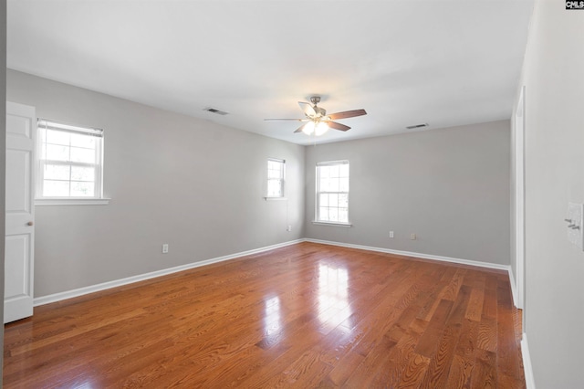 unfurnished room with ceiling fan, wood finished floors, visible vents, and baseboards