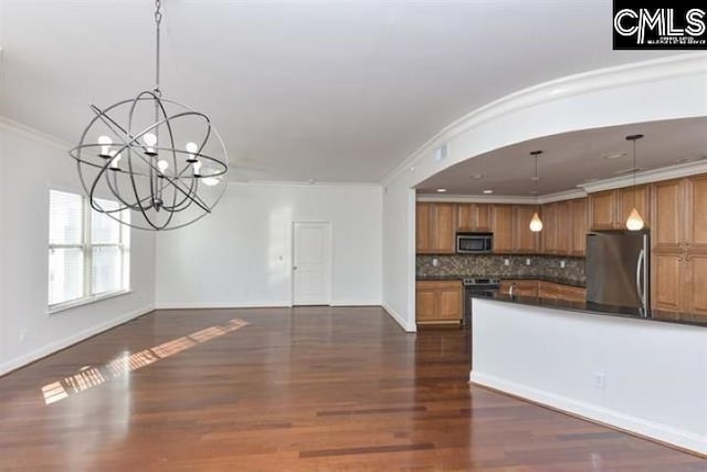 kitchen with dark countertops, appliances with stainless steel finishes, brown cabinets, open floor plan, and hanging light fixtures