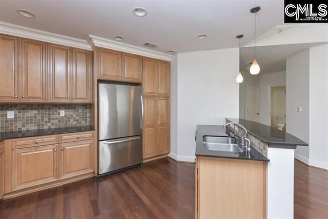 kitchen with tasteful backsplash, dark countertops, freestanding refrigerator, hanging light fixtures, and a sink