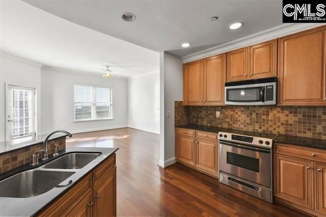 kitchen featuring dark countertops, backsplash, appliances with stainless steel finishes, open floor plan, and a sink