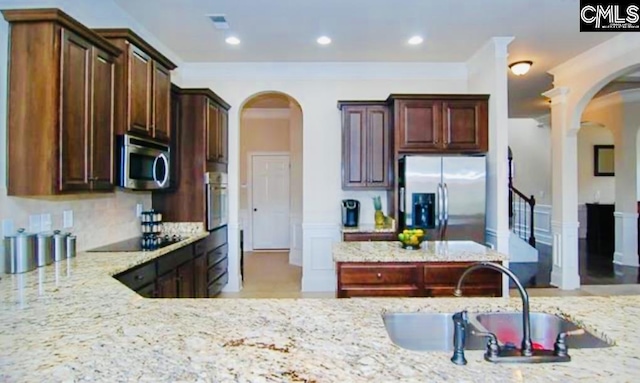 kitchen featuring arched walkways, appliances with stainless steel finishes, light stone counters, a sink, and recessed lighting