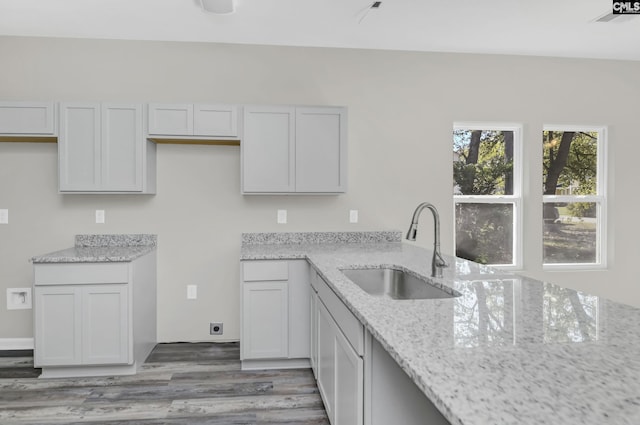 kitchen with light stone countertops, white cabinets, a sink, and wood finished floors