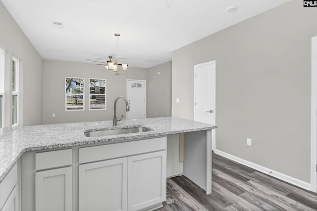 kitchen with baseboards, light stone counters, a sink, and white cabinets