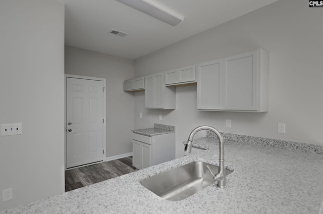 kitchen with dark wood-style floors, visible vents, white cabinetry, a sink, and light stone countertops