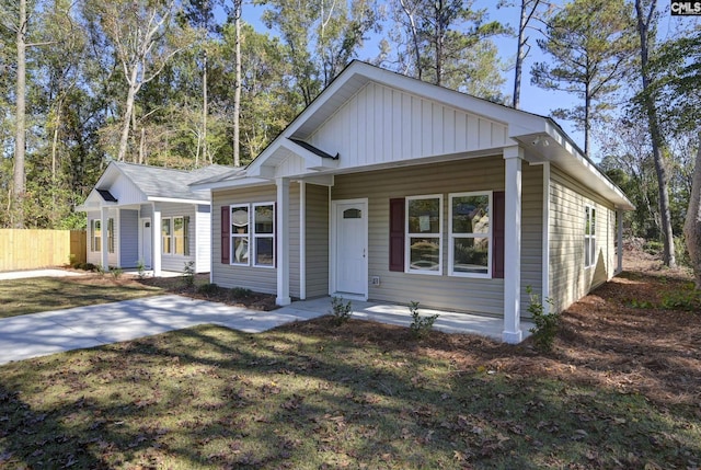 view of front of house with board and batten siding, a front yard, and fence