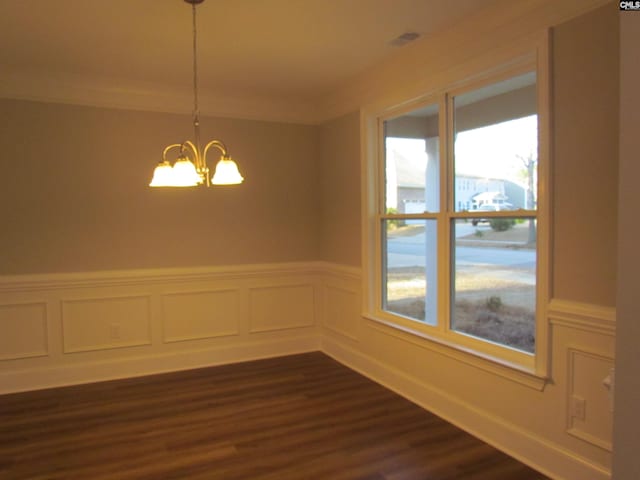 empty room with dark wood-type flooring, a chandelier, wainscoting, and crown molding