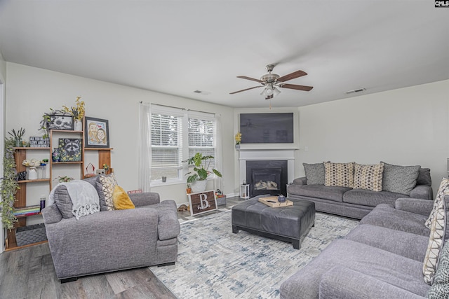 living room with a glass covered fireplace, visible vents, ceiling fan, and wood finished floors