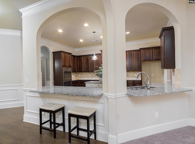 kitchen featuring light stone counters, a sink, decorative backsplash, and dark brown cabinets