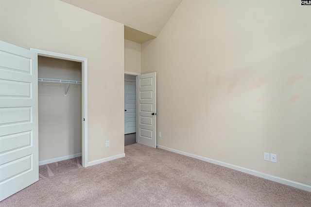 unfurnished bedroom with baseboards, vaulted ceiling, a closet, and light colored carpet