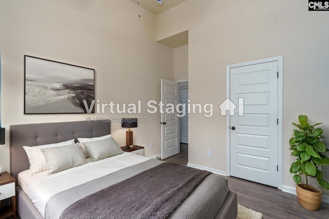 bedroom with dark wood-type flooring, a towering ceiling, and baseboards