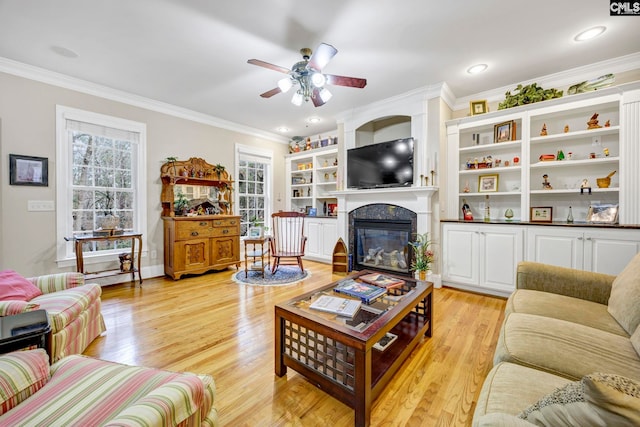 living room featuring light wood finished floors, a glass covered fireplace, a ceiling fan, and crown molding