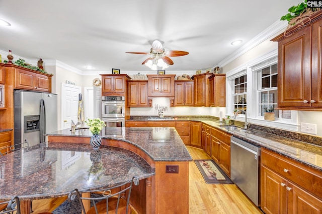 kitchen featuring a breakfast bar, a center island with sink, appliances with stainless steel finishes, a sink, and dark stone counters