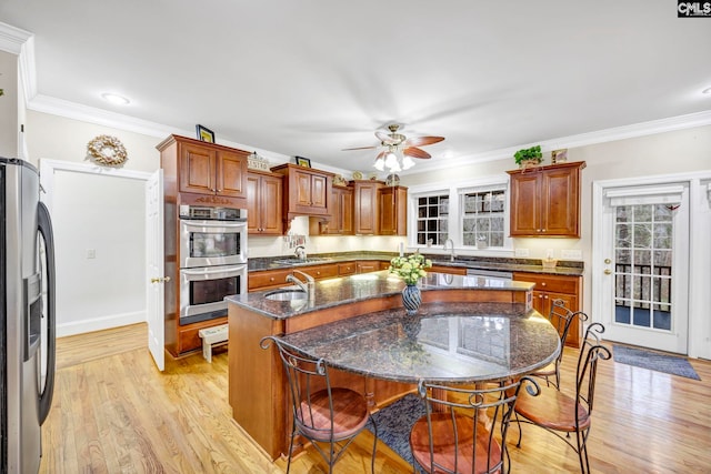 kitchen featuring an island with sink, light wood-style flooring, dark stone counters, and stainless steel appliances