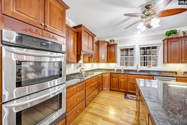 kitchen with crown molding, stainless steel appliances, brown cabinetry, light wood-style floors, and dark stone counters