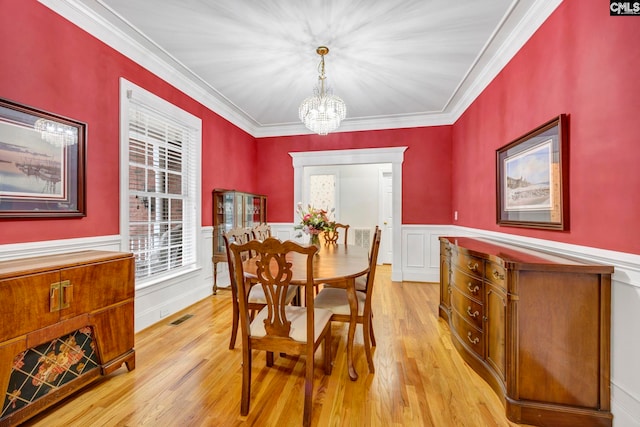 dining space featuring light wood finished floors, wainscoting, visible vents, and crown molding