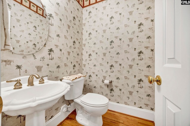 bathroom featuring toilet, a sink, wood finished floors, baseboards, and wallpapered walls