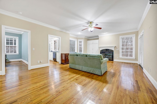 living room featuring ornamental molding, a glass covered fireplace, baseboards, and light wood finished floors