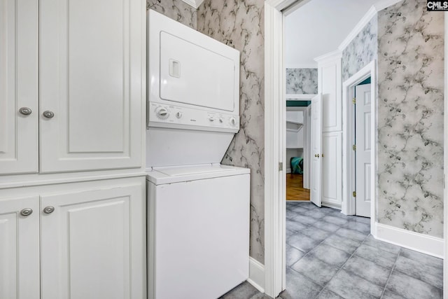 washroom featuring laundry area, baseboards, stacked washing maching and dryer, and wallpapered walls