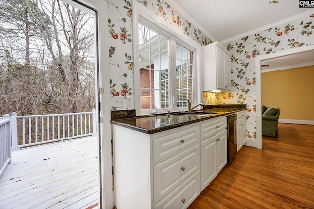 kitchen featuring white cabinetry, light wood-style floors, wallpapered walls, dark stone countertops, and crown molding