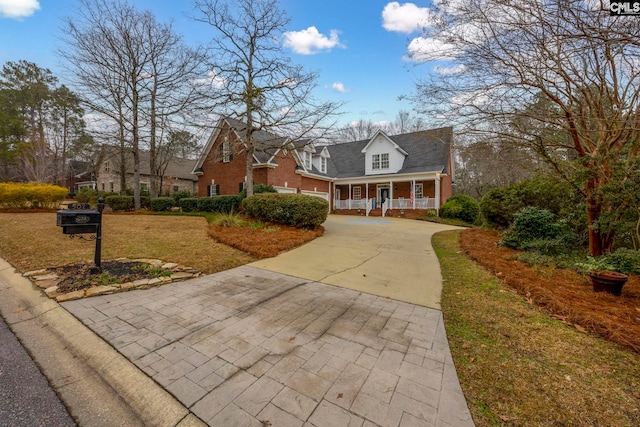 cape cod house with a porch, concrete driveway, brick siding, and a front lawn