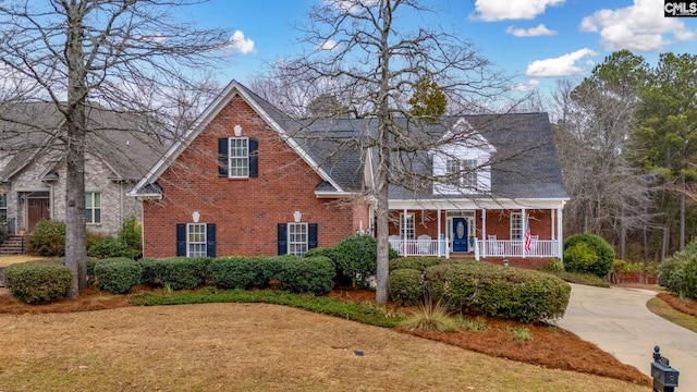 traditional-style house with covered porch, a front lawn, and brick siding