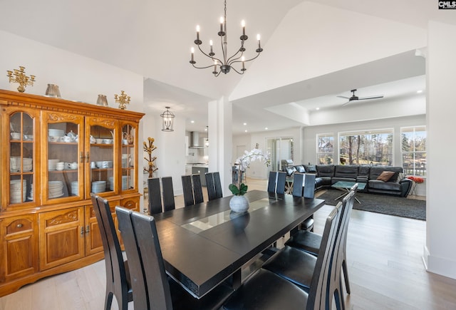 dining space with light wood-style floors, high vaulted ceiling, and ceiling fan with notable chandelier