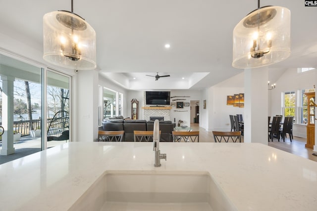 kitchen with light stone counters, pendant lighting, a fireplace, a raised ceiling, and open floor plan