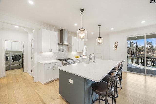 kitchen featuring light countertops, white cabinetry, a sink, separate washer and dryer, and wall chimney exhaust hood