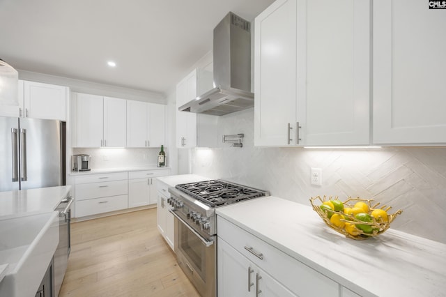 kitchen featuring white cabinets, wall chimney range hood, high quality appliances, and light countertops