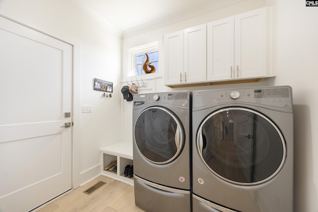 laundry room with visible vents, light wood-style floors, ornamental molding, cabinet space, and washing machine and clothes dryer