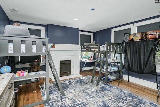 bedroom featuring light wood-type flooring, a brick fireplace, visible vents, and baseboards