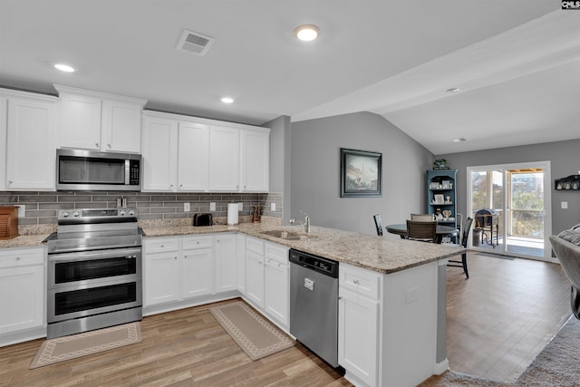 kitchen featuring stainless steel appliances, a peninsula, a sink, visible vents, and vaulted ceiling