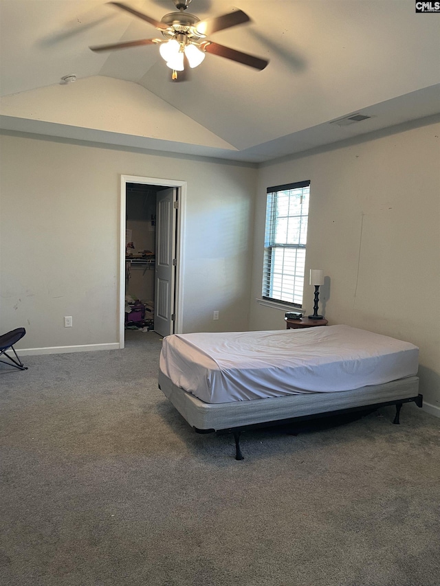 carpeted bedroom featuring a ceiling fan, visible vents, vaulted ceiling, baseboards, and a walk in closet