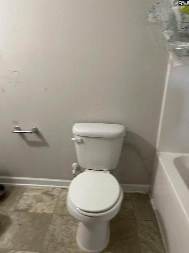 bathroom with toilet, a bathing tub, and baseboards