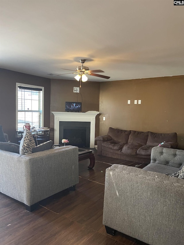 living area with dark wood-style flooring, a fireplace with raised hearth, and ceiling fan