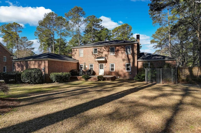 rear view of house with roof mounted solar panels, brick siding, fence, and a chimney