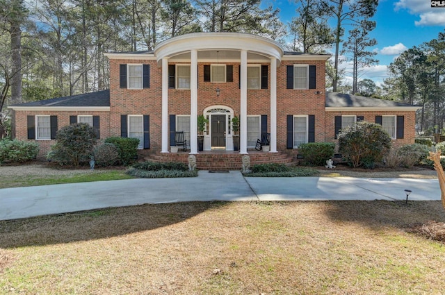 neoclassical / greek revival house featuring a porch, brick siding, and a front lawn