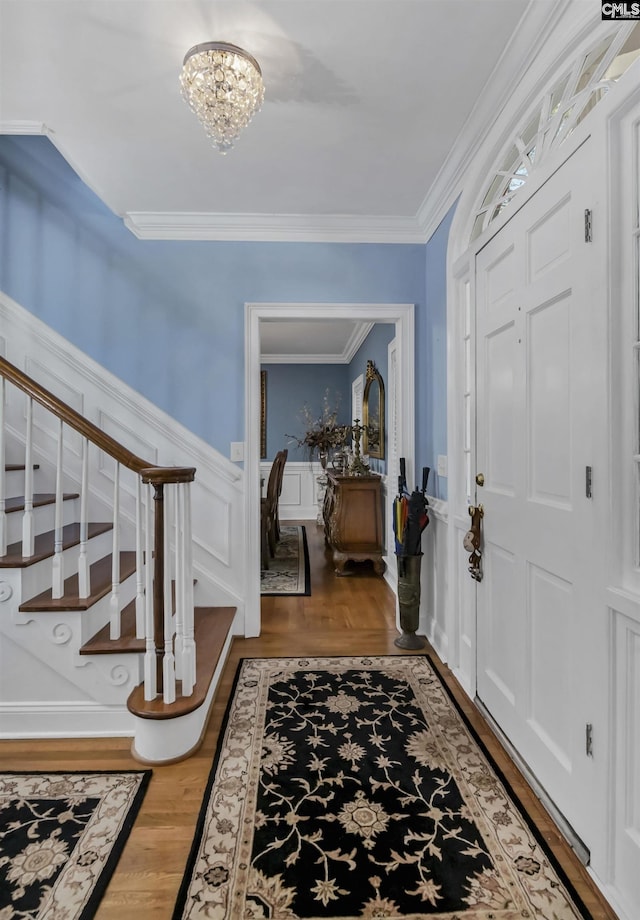 foyer entrance featuring a notable chandelier, a wainscoted wall, light wood-style floors, stairway, and crown molding