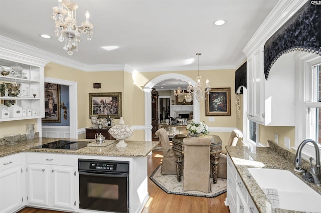 kitchen with white cabinets, black appliances, a fireplace, a chandelier, and a sink