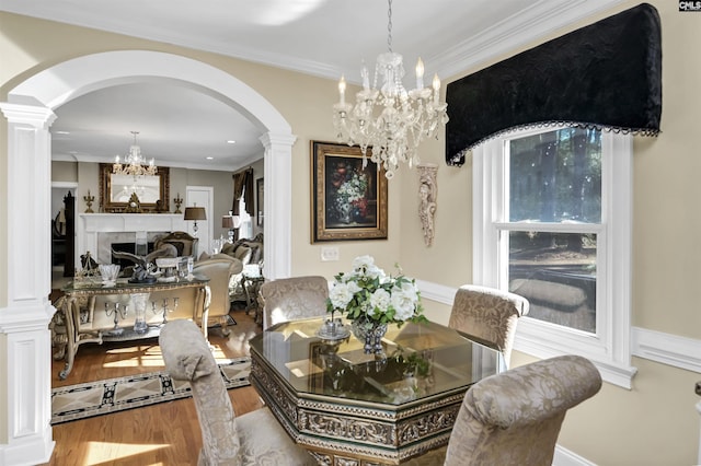 dining room featuring wood finished floors, crown molding, ornate columns, a fireplace, and a notable chandelier