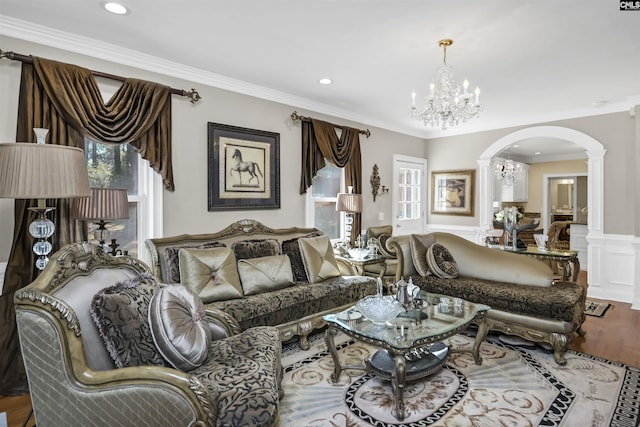 living area with arched walkways, a wainscoted wall, decorative columns, ornamental molding, and wood finished floors