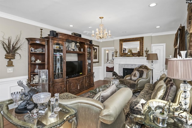 living room featuring a wainscoted wall, a fireplace, wood finished floors, ornamental molding, and an inviting chandelier