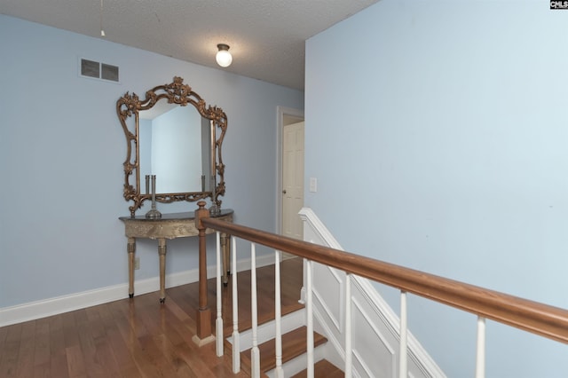 corridor with a textured ceiling, wood finished floors, visible vents, and baseboards