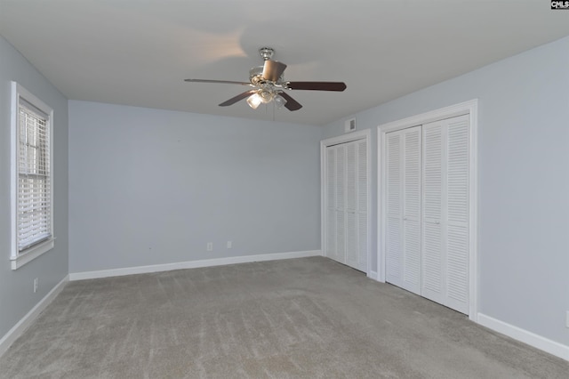 unfurnished bedroom with carpet floors, visible vents, baseboards, and multiple closets