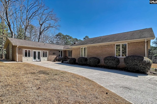 rear view of house with concrete driveway, a patio, a lawn, french doors, and brick siding