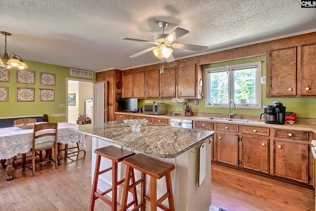 kitchen featuring light wood-style floors, visible vents, brown cabinetry, and a sink