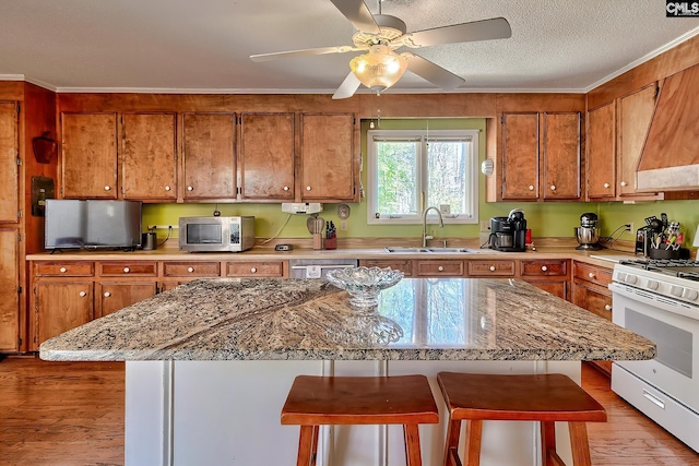 kitchen featuring white gas stove, brown cabinetry, stainless steel microwave, and a sink