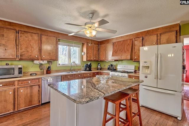 kitchen with light wood finished floors, custom range hood, brown cabinets, stainless steel appliances, and a sink