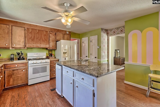 kitchen featuring hardwood / wood-style flooring, white appliances, a textured ceiling, and wallpapered walls