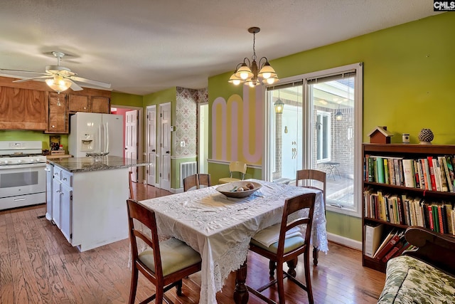 dining space featuring visible vents, wallpapered walls, hardwood / wood-style floors, baseboards, and ceiling fan with notable chandelier